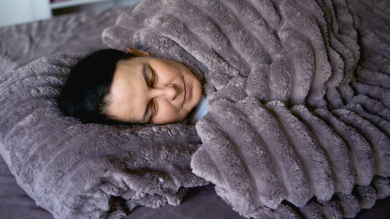 close up shot of person laying inside a gray weighted blanket with striped stitching