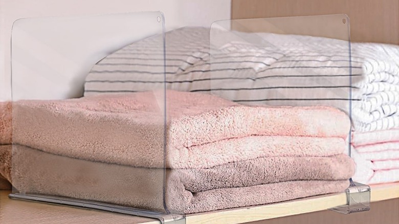 clear acrylic shelf dividers that are attached to a white shelf with light neutral towels and sheets